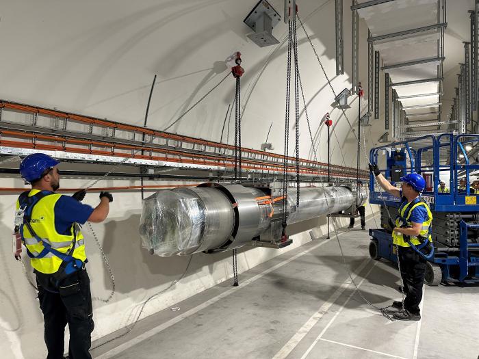 Two workers lifting a metallic pipe in the UR underground gallery